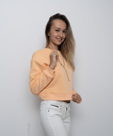 Modelka w krótkiej bluzie crop top w kolorze soczystej brzoskwini, uszytej z bawełny premium z misiowym wnętrzem – produkt Kadora Studio.