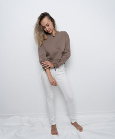 Modelka w krótkiej bluzie crop top w kolorze taupe, uszytej z bawełny premium z misiowym wnętrzem. Dopasowany fason podkreśla talię – produkt Kadora Studio.