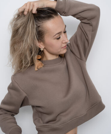 Modelka w krótkiej bluzie crop top w kolorze taupe, uszytej z bawełny premium z misiowym wnętrzem. Dopasowany fason podkreśla talię – produkt Kadora Studio.